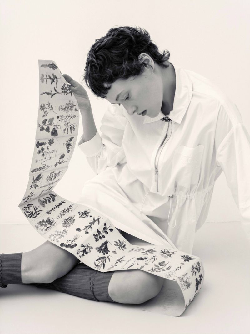 Model in white shirt holding a long illustrated botanical paper scroll against a light studio backdrop