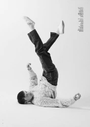 Monochrome fashion editorial image of a male model lying down with legs raised against a white studio background.