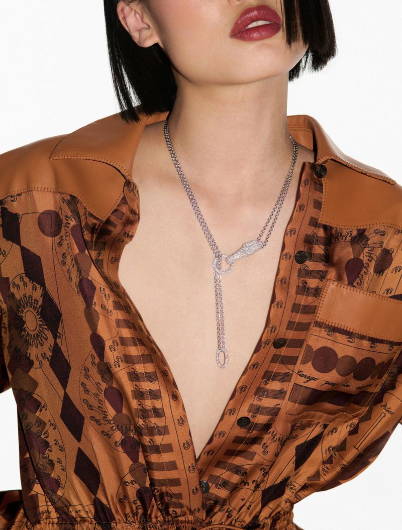 Woman wearing a brown patterned shirt and a silver necklace posing against a white backdrop in a studio setting.