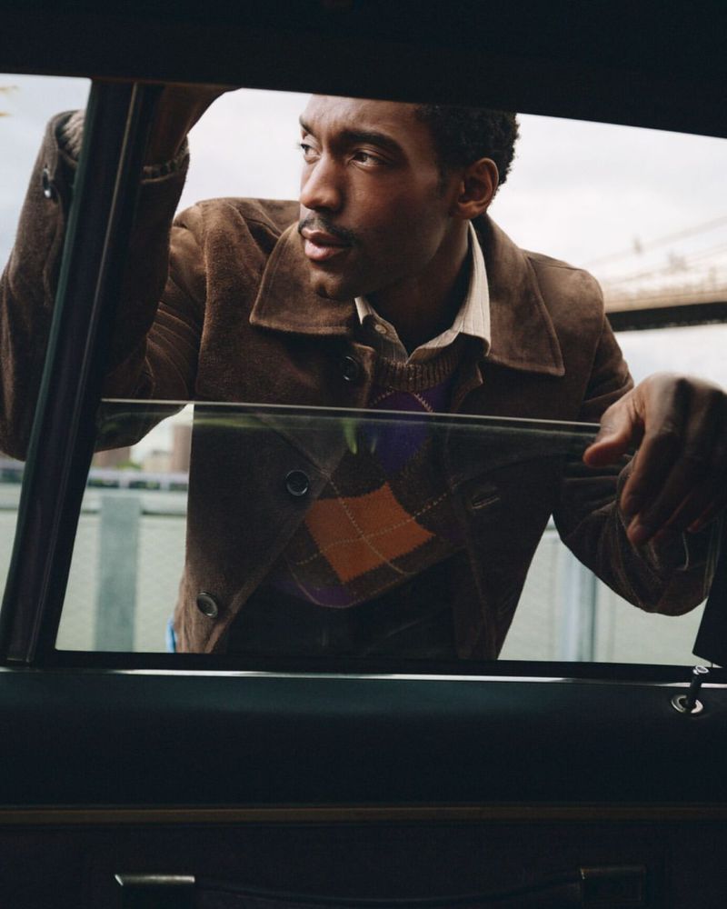 Man wearing a brown suede jacket and argyle sweater leaning into a car window