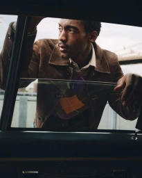 Man wearing a brown suede jacket and argyle sweater leaning into a car window