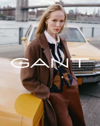 Model leaning against a yellow car near a waterfront with a bridge in the background for Gant Fall/Winter 2026.