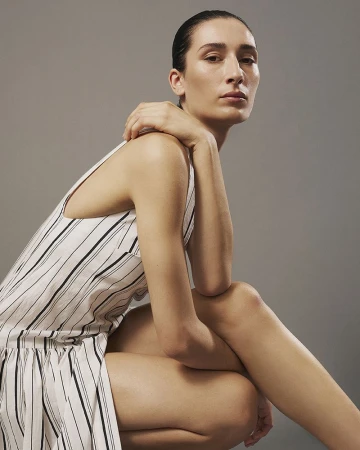 Model in a striped dress crouching against a neutral grey studio backdrop for Eudon Choi SS27