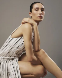 Model in a striped dress crouching against a neutral grey studio backdrop for Eudon Choi SS27
