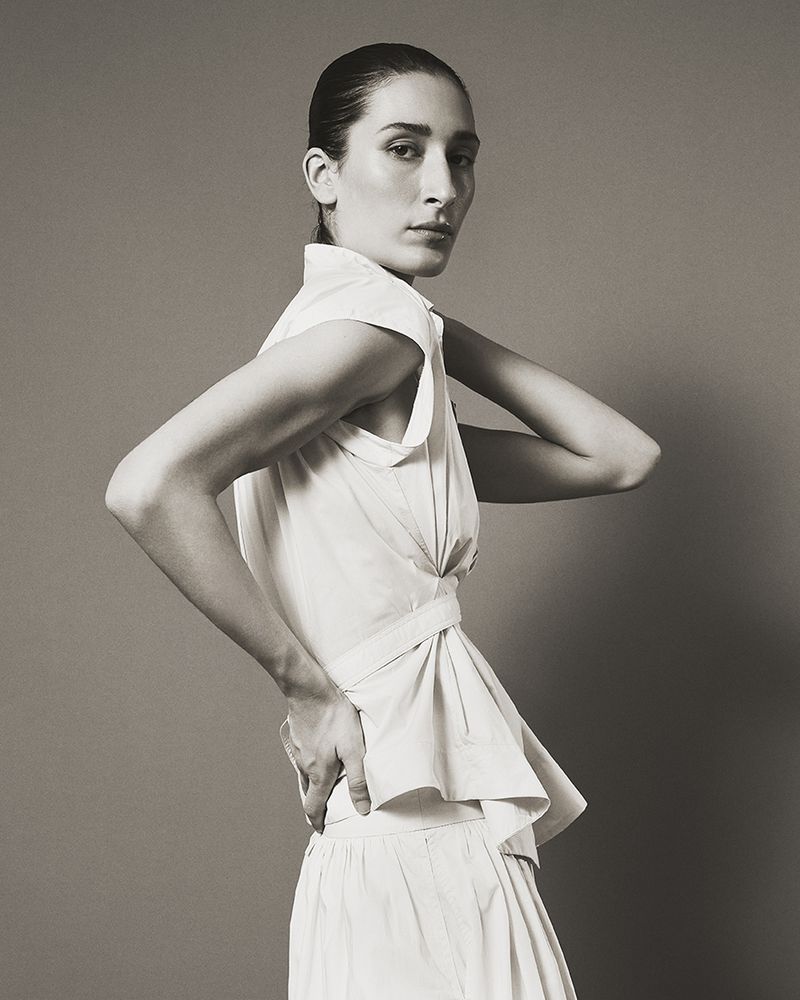 Model in white sleeveless button-down shirt and skirt posing against a neutral studio backdrop for Eudon Choi SS27