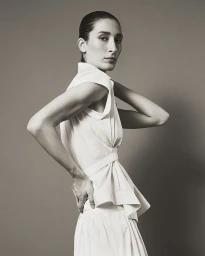 Model in white sleeveless button-down shirt and skirt posing against a neutral studio backdrop for Eudon Choi SS27