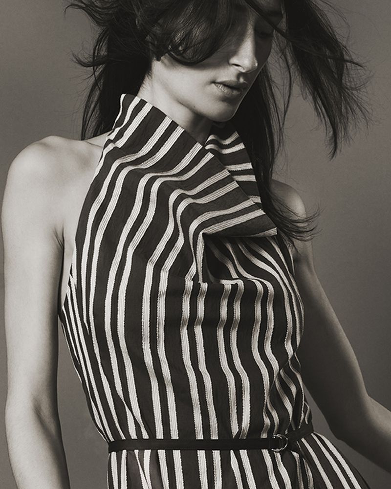 Model wearing a black and white striped sleeveless top with high folded collar against a neutral backdrop.