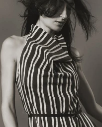 Model wearing a black and white striped sleeveless top with high folded collar against a neutral backdrop.