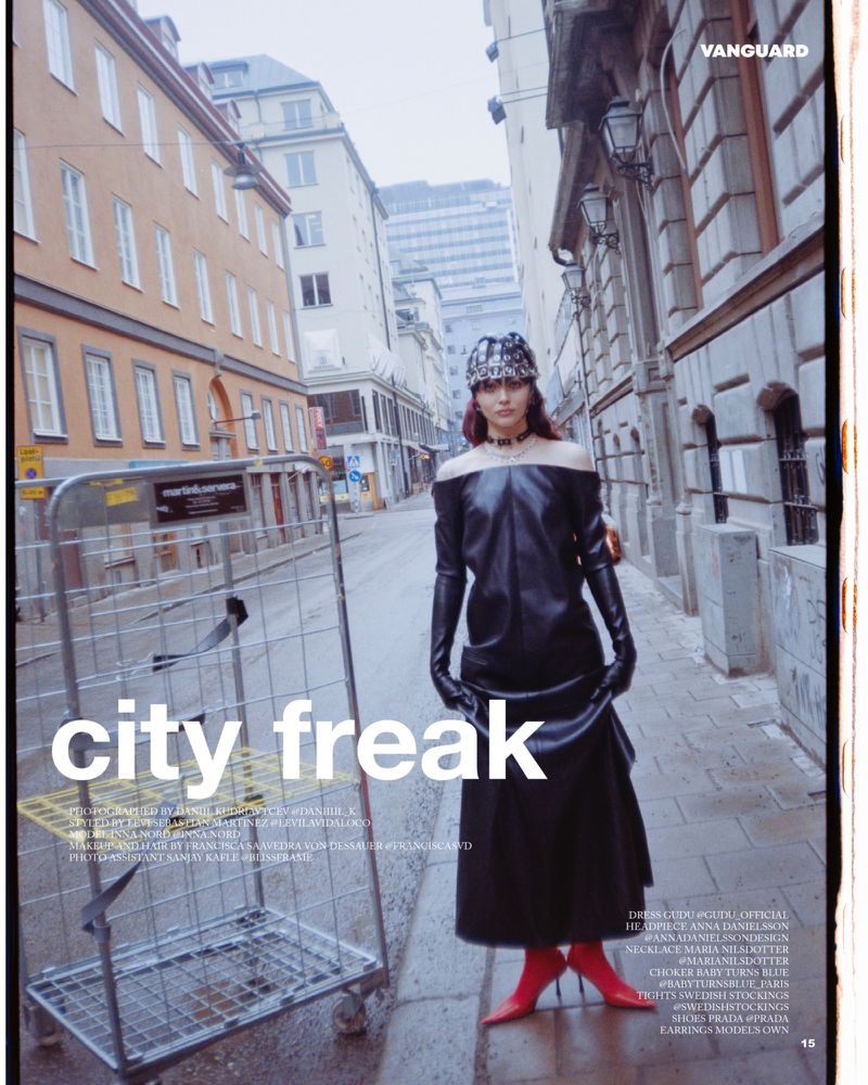 Editorial fashion shot of a woman in a black dress and red boots, standing on a city street, with a metal cart beside her.