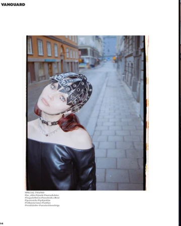 A stylish woman in an off-shoulder top and head covering poses on a city street with aged buildings and cobblestone pavement.