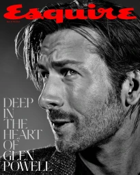 Close-up monochrome portrait of Glen Powell with dark stubble against a grey background for Esquire magazine cover.