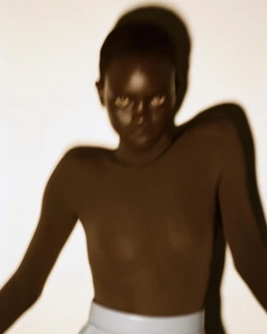 Model Anok Yai in dark fitted top casting a shadow against a white wall for Alaia