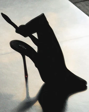 Close-up of a black stiletto high heel shoe resting on a reflective metallic surface with a sharp shadow.
