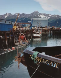 Fishing boat Nushagak docked in a harbor with snow-capped mountains in the background