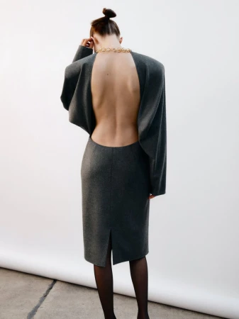 Model wearing a grey open-back dress with a gold chain necklace viewed from behind against a white seamless background