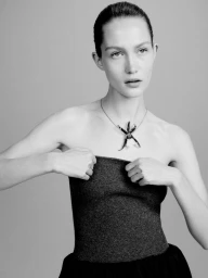 Model Vika Evseeva wearing a dark strapless top and star-shaped pendant necklace against a grey seamless studio background.
