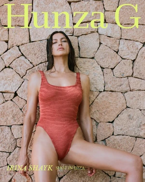 Model Irina Shayk wearing a red textured one-piece swimsuit against a dry stone wall for Hunza G Resort 2027 campaign.