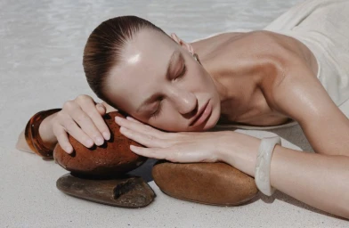 Model resting head on smooth brown stones wearing a white top and resin bracelets