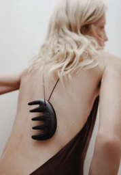 Model with long blonde hair seen from behind wearing a dark pendant necklace against a plain white wall