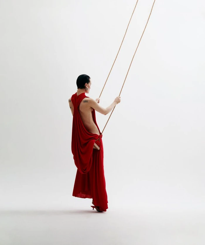 Model in a red backless dress standing and holding ropes against a white background