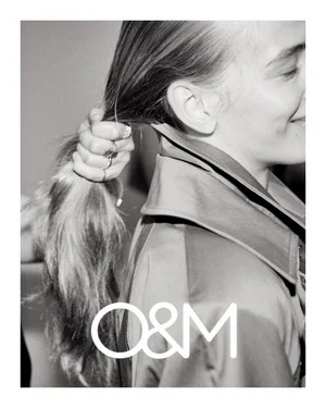 Close-up black and white portrait of a person holding their long hair in a ponytail while wearing a collared coat.