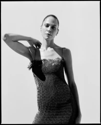 Model in a dark slip dress with lace trim posing against a plain background in a black and white fashion portrait.
