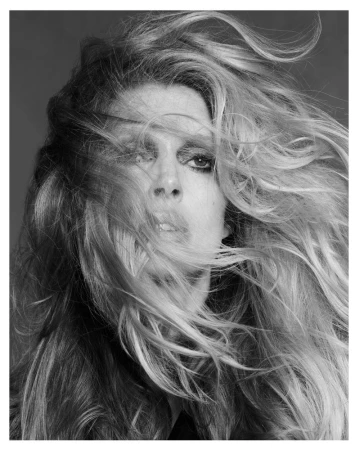 Close-up portrait of model Iselin Steiro with long blonde hair blowing across her face in a monochrome studio setting