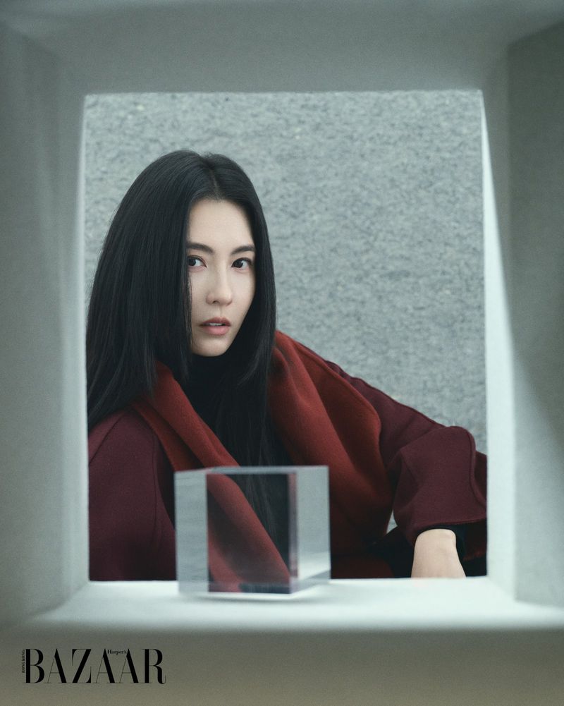 Cecilia Cheung framed in architectural cutout wearing burgundy coat for Harper's Bazaar