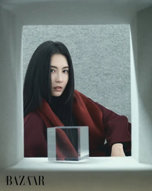 Cecilia Cheung framed in architectural cutout wearing burgundy coat for Harper's Bazaar