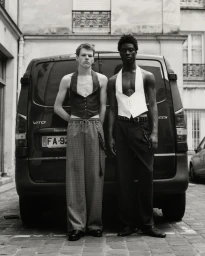 Two male models standing in front of a black van wearing sleeveless waistcoats and trousers for Paris Men SS26.