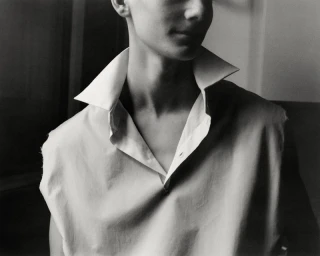 Close-up of a person wearing an open-collared white shirt captured in a monochrome photographic portrait.