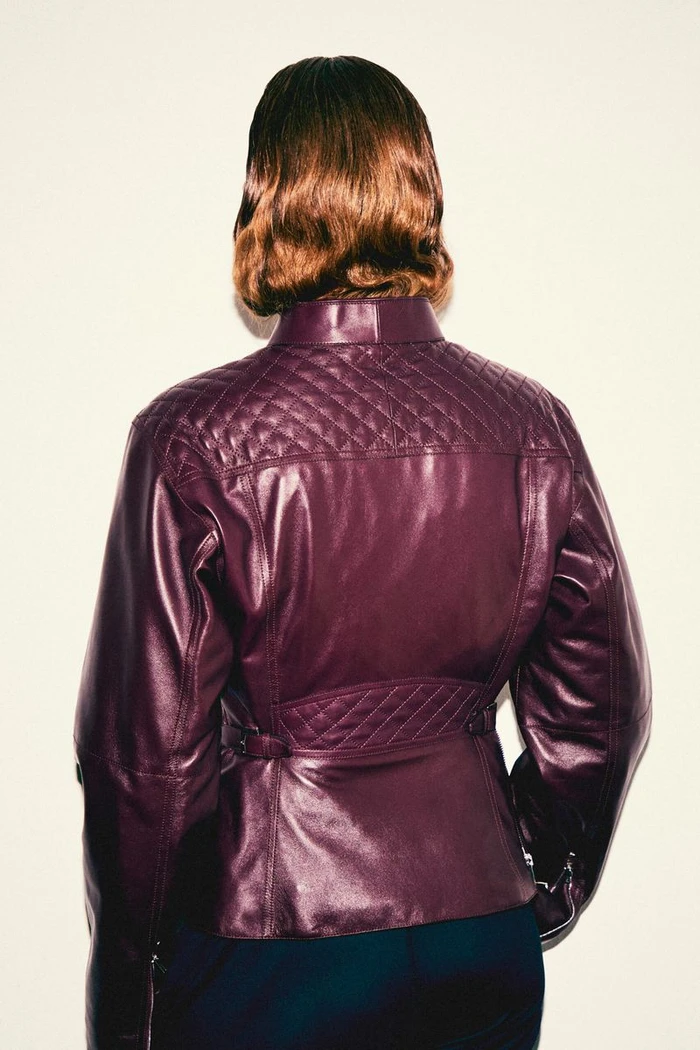 Woman seen from behind wearing a plum quilted leather jacket against a neutral studio background