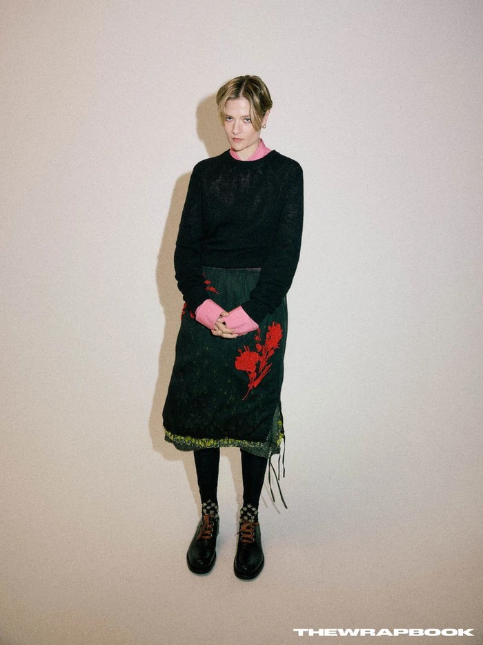 Louisa Jacobson posing against a plain neutral backdrop wearing a dark sweater over a patterned skirt