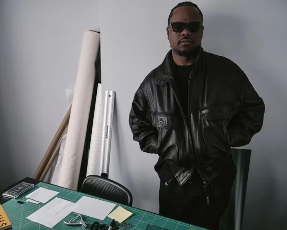 Man wearing sunglasses and a black leather jacket standing in a studio with drafting materials