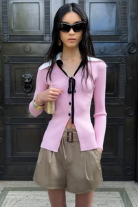 Model in pink collared cardigan and brown shorts standing before dark double doors