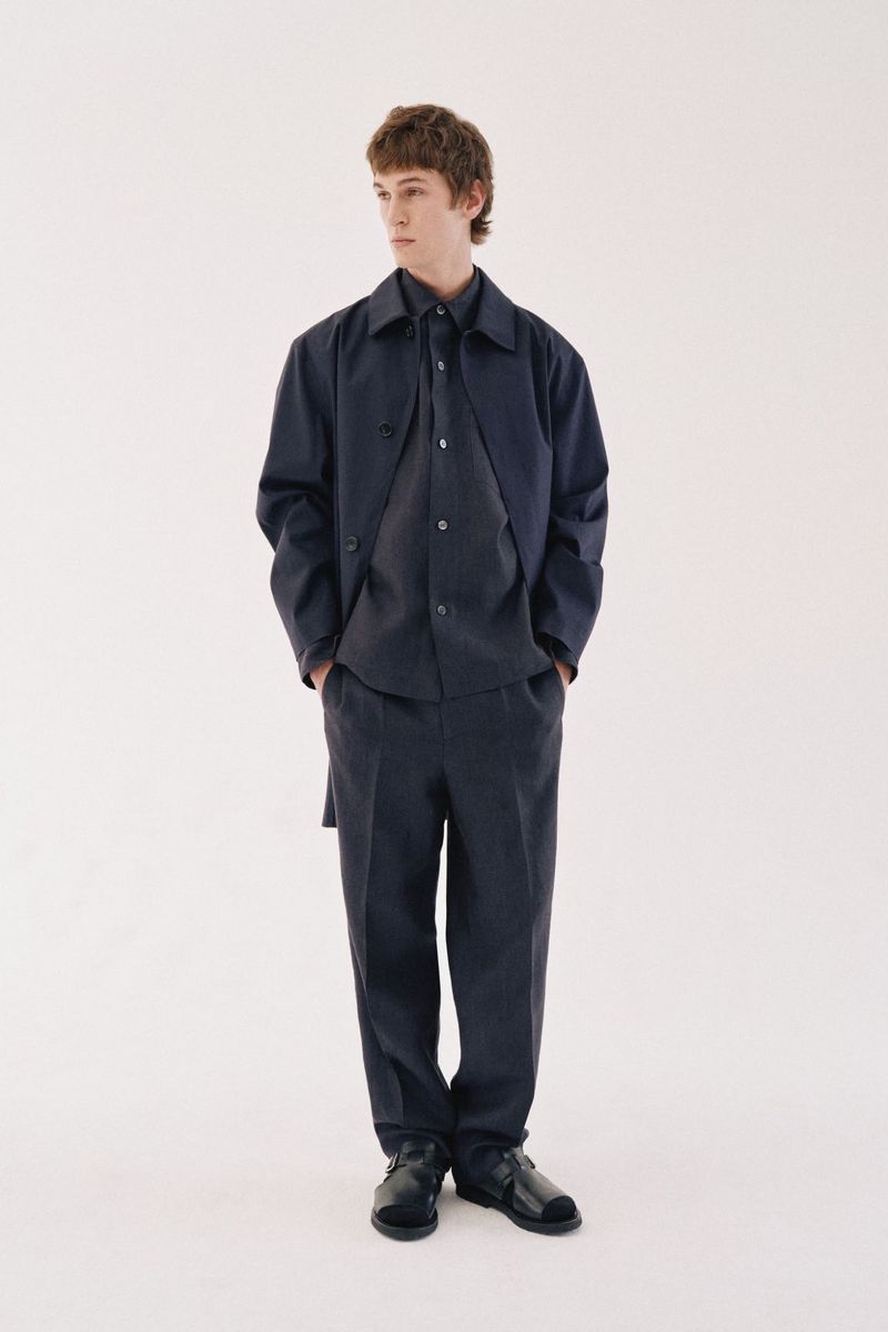 Model wearing a dark navy jacket and trousers standing against a plain white background for Margaret Howell