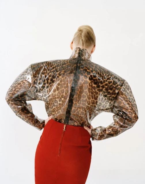 Woman poses in a transparent leopard print top and red pencil skirt against a white backdrop in a studio setting. Fashion editorial shot.
