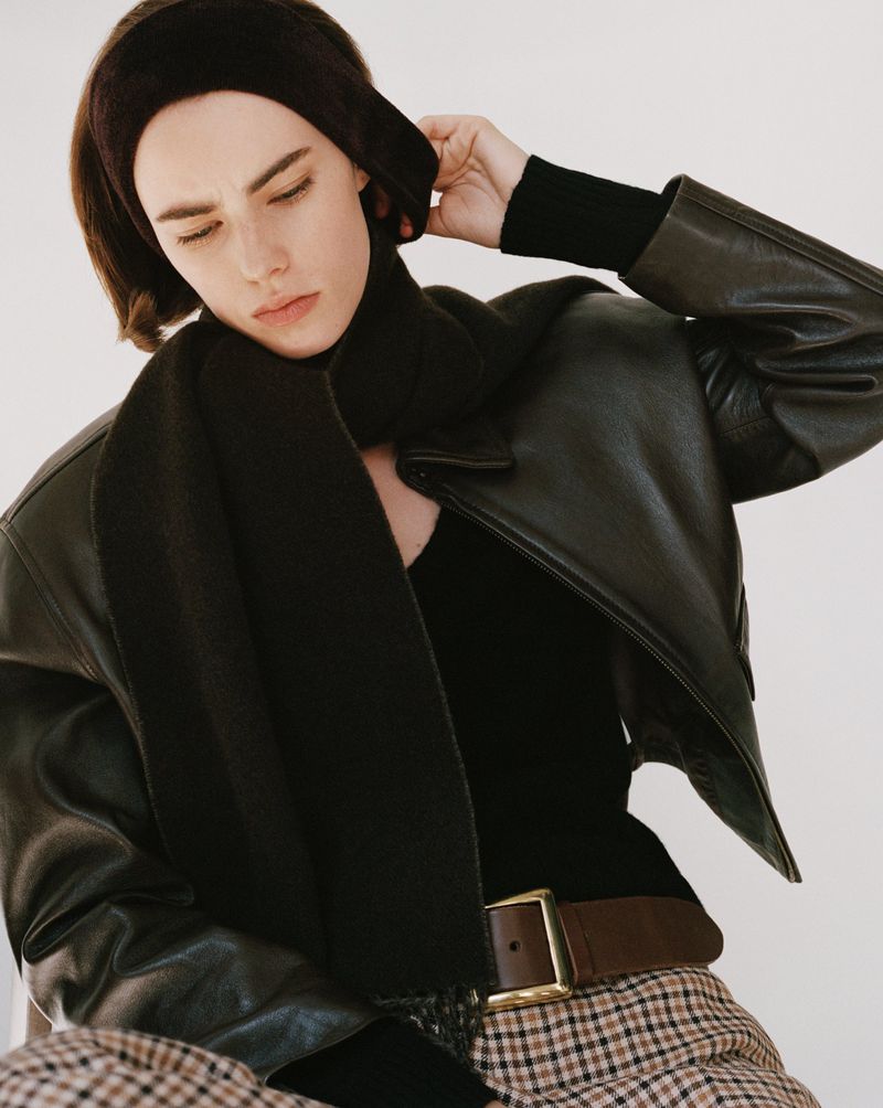 Model wearing a black leather jacket, dark scarf, headband, and houndstooth trousers against a white seamless background.