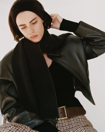 Model wearing a black leather jacket, dark scarf, headband, and houndstooth trousers against a white seamless background.