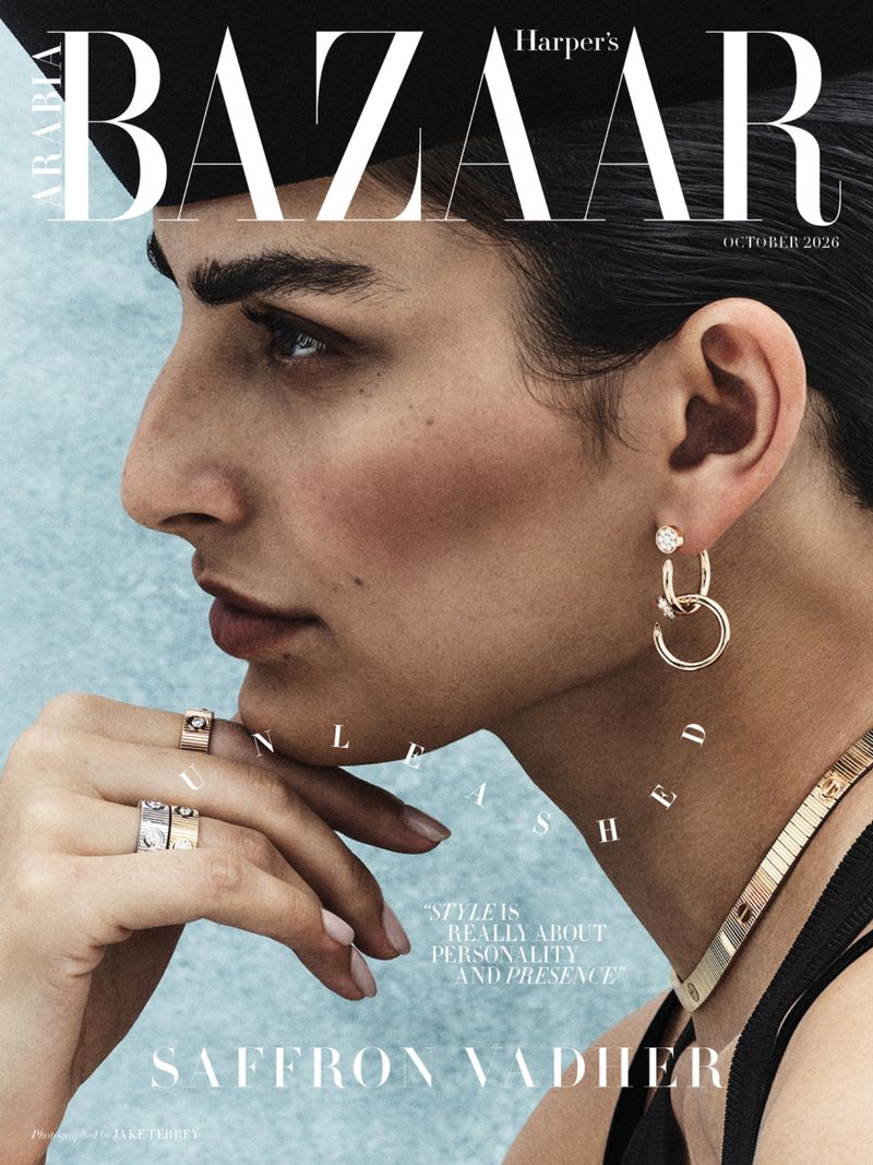 Close-up profile portrait of model Saffron Vadher wearing jewelry and a black outfit against a textured blue background