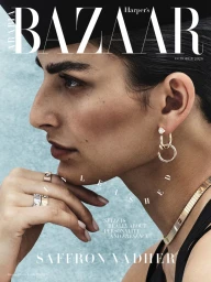 Close-up profile portrait of model Saffron Vadher wearing jewelry and a black outfit against a textured blue background