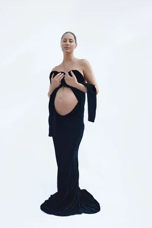 Pregnant woman wearing a strapless black velvet evening gown against a plain white studio background