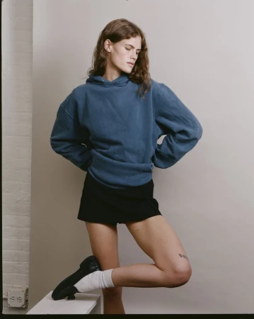 Model wearing a blue hoodie and black shorts with white socks and loafers posing against a neutral studio backdrop