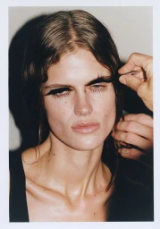 Close-up portrait of a woman receiving dramatic makeup application with false eyelashes for Lucia B Richardson