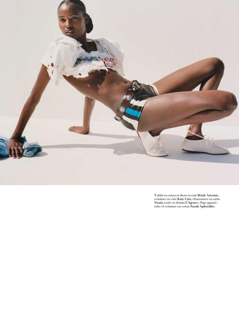 Fashion shot of Black female model in a pose on a white surface, wearing a white crop top, print shorts, and off-white shoes.