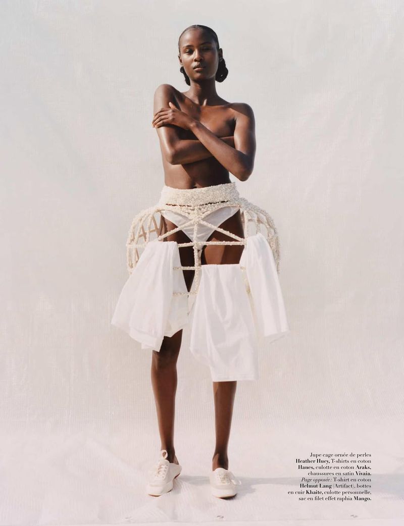 Fashion editorial shot of a slender adult woman in a white setting. She wears a crocheted cage skirt with white clothes hangers.