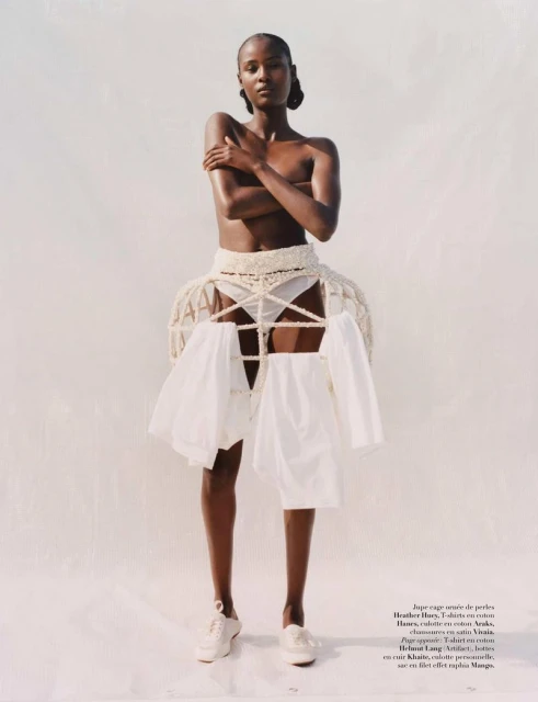 Fashion editorial shot of a slender adult woman in a white setting. She wears a crocheted cage skirt with white clothes hangers.