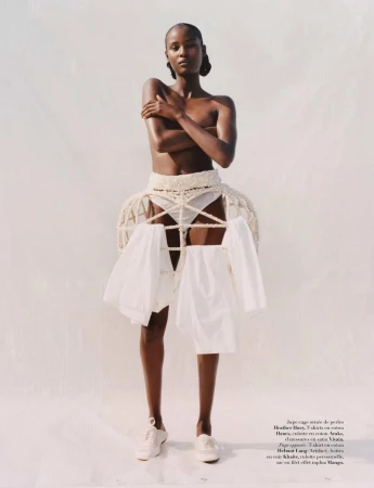 Fashion editorial shot of a slender adult woman in a white setting. She wears a crocheted cage skirt with white clothes hangers.