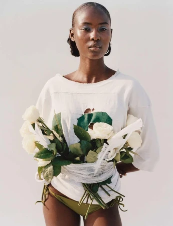 Striking portrait of a Black woman in a white top and bikini bottom, holding white roses against a clean white backdrop.