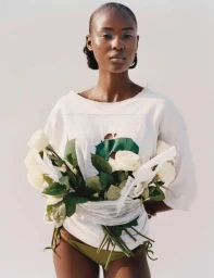 Model Layla Etengan wearing a distressed white t-shirt with white roses bound to her waist against a pale backdrop.